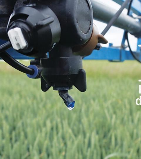 Sproeiarm van landbouwmachine boven groen gewas, tekst “Pendant le désherbage”