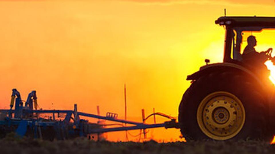 Tractor op veld bij zonsondergang, silhouet tegen oranje lucht
