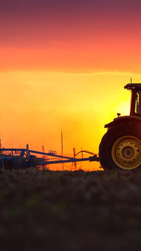 Tractor op veld bij zonsondergang, silhouet tegen oranje lucht