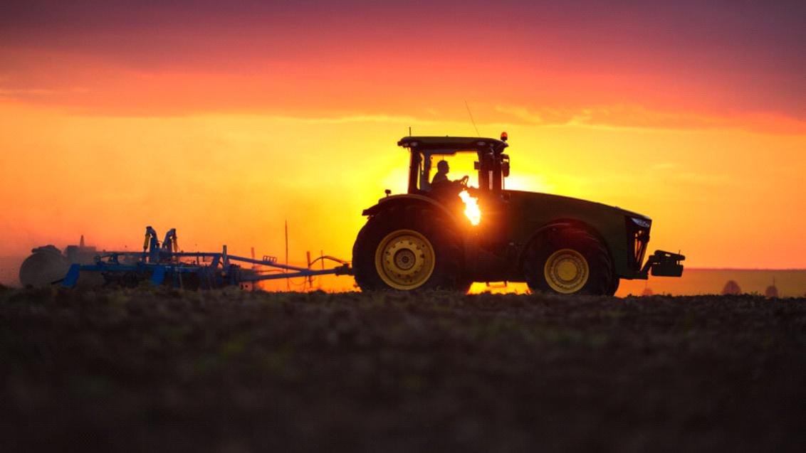 Silhouet van tractor bij zonsondergang op akker, oranje lucht