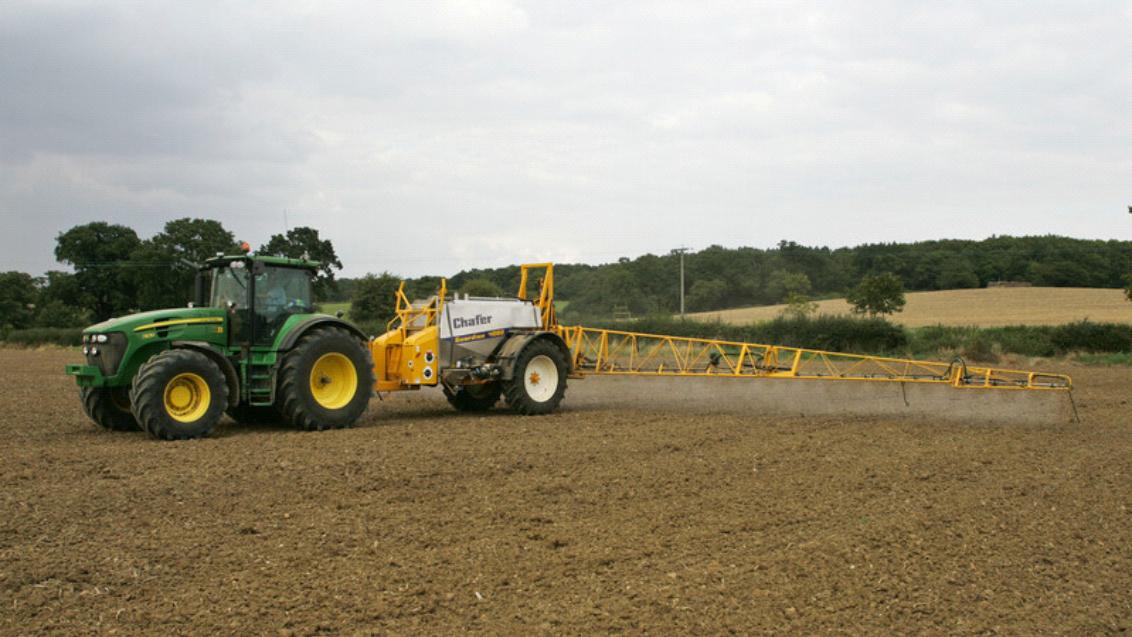 Groene tractor met gele zaaiwagen op akker onder bewolkte lucht